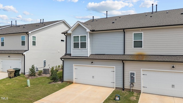 rear view of house featuring a garage, central air condition unit, and a lawn