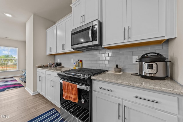 kitchen featuring light wood-type flooring, appliances with stainless steel finishes, light stone counters, and white cabinets