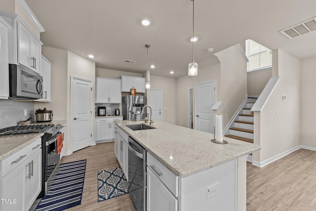 kitchen featuring stainless steel appliances, hanging light fixtures, sink, an island with sink, and white cabinets