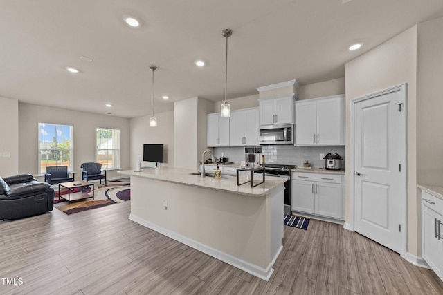 kitchen with white cabinetry, light hardwood / wood-style floors, decorative light fixtures, and a center island with sink