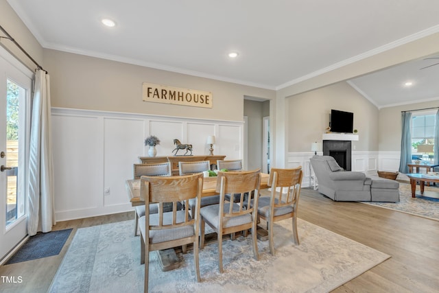 dining area featuring lofted ceiling, a fireplace, light wood-type flooring, and crown molding