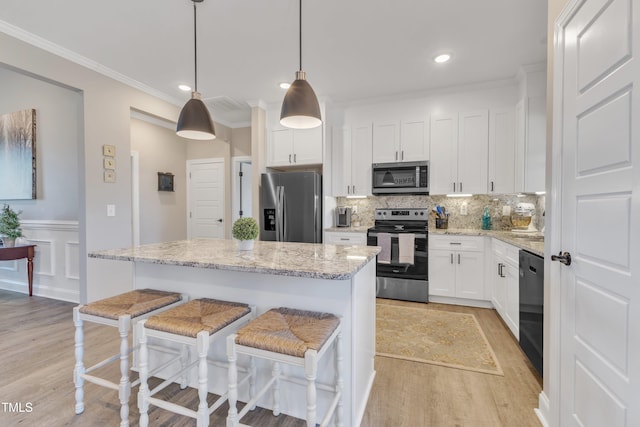 kitchen featuring appliances with stainless steel finishes, light stone countertops, a kitchen island, white cabinets, and decorative light fixtures