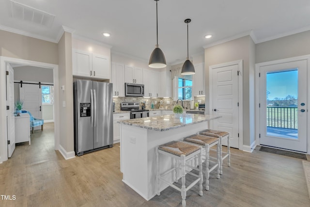 kitchen featuring white cabinetry, a barn door, light stone countertops, a kitchen island, and appliances with stainless steel finishes