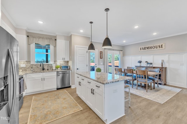 kitchen featuring light stone countertops, hanging light fixtures, a kitchen island, white cabinetry, and appliances with stainless steel finishes