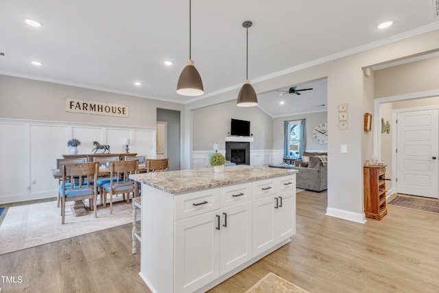 kitchen featuring light stone counters, pendant lighting, a kitchen island, white cabinetry, and ceiling fan