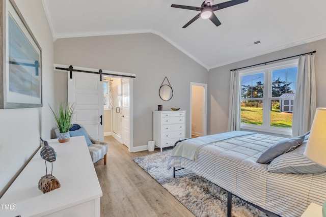 bedroom featuring vaulted ceiling, connected bathroom, light wood-type flooring, a barn door, and ceiling fan