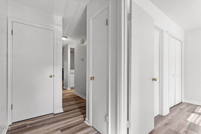 corridor with light hardwood / wood-style floors and a textured ceiling