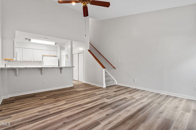 unfurnished living room with light hardwood / wood-style floors, ceiling fan, and a towering ceiling