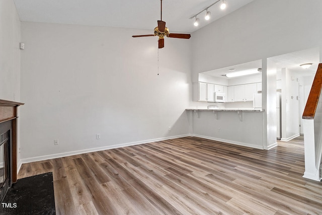 unfurnished living room with light hardwood / wood-style floors, ceiling fan, and high vaulted ceiling