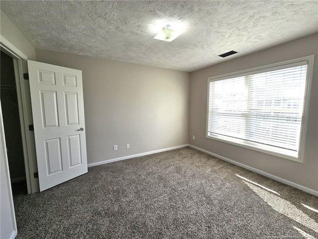 unfurnished room with a textured ceiling and dark carpet