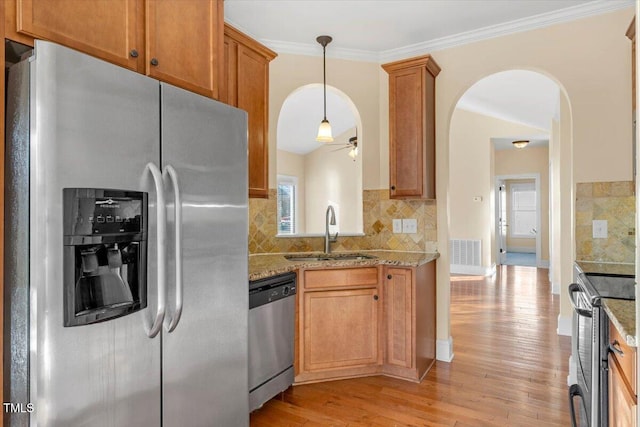 kitchen featuring appliances with stainless steel finishes, backsplash, light stone counters, sink, and light hardwood / wood-style floors