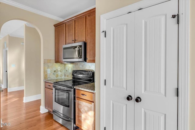 kitchen with light wood-type flooring, tasteful backsplash, light stone counters, stainless steel appliances, and crown molding