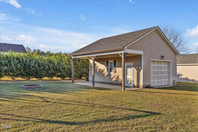 back of property with an outbuilding, a garage, a yard, and an outdoor fire pit