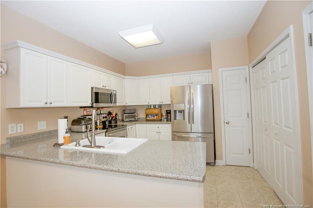 kitchen with light stone countertops, white cabinetry, stainless steel appliances, kitchen peninsula, and light tile patterned floors