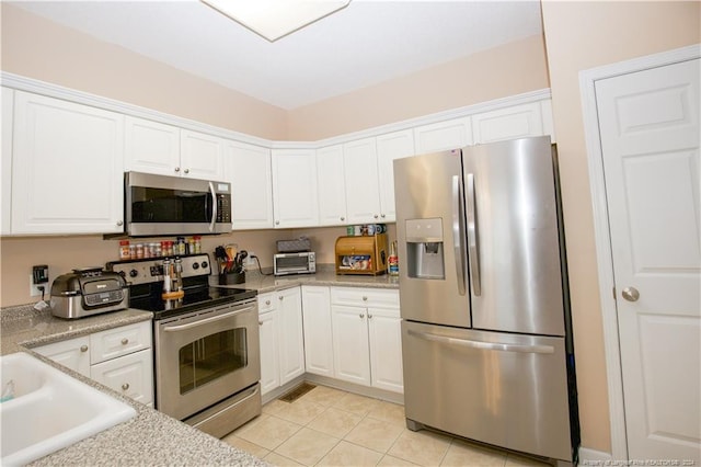 kitchen with light stone countertops, light tile patterned floors, white cabinetry, and appliances with stainless steel finishes