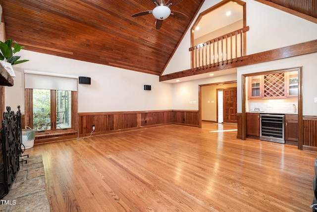 unfurnished living room with beverage cooler, high vaulted ceiling, wood walls, wood ceiling, and light wood-type flooring