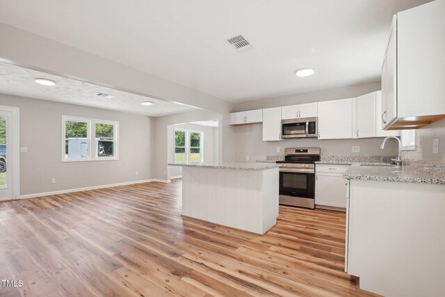 kitchen with light hardwood / wood-style floors, stainless steel appliances, white cabinets, sink, and a kitchen island