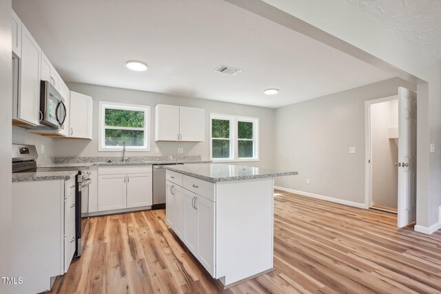 kitchen with light hardwood / wood-style floors, white cabinetry, a kitchen island, and appliances with stainless steel finishes