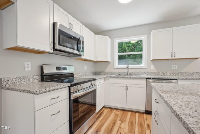 kitchen featuring white cabinetry, sink, light stone counters, appliances with stainless steel finishes, and light hardwood / wood-style flooring