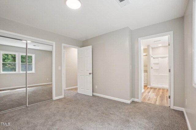 unfurnished bedroom with light colored carpet, connected bathroom, and a closet