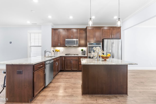 kitchen featuring pendant lighting, light hardwood / wood-style floors, a kitchen bar, kitchen peninsula, and stainless steel appliances