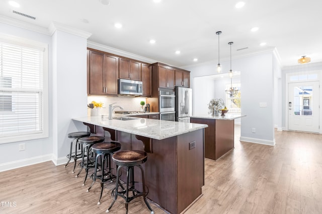 kitchen with hanging light fixtures, light stone counters, appliances with stainless steel finishes, a kitchen bar, and kitchen peninsula