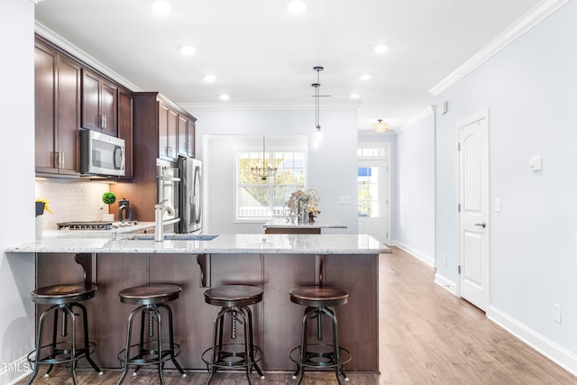 kitchen featuring light stone counters, stainless steel appliances, decorative light fixtures, and ornamental molding