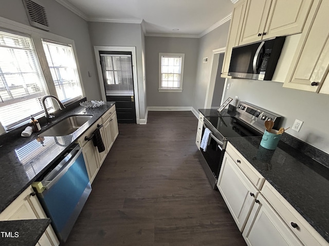 kitchen with sink, dark stone countertops, ornamental molding, appliances with stainless steel finishes, and dark hardwood / wood-style flooring