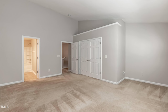 unfurnished bedroom featuring ensuite bathroom, a closet, high vaulted ceiling, and light colored carpet