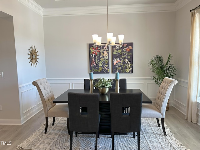 dining area featuring a chandelier, light wood-type flooring, a wainscoted wall, and crown molding