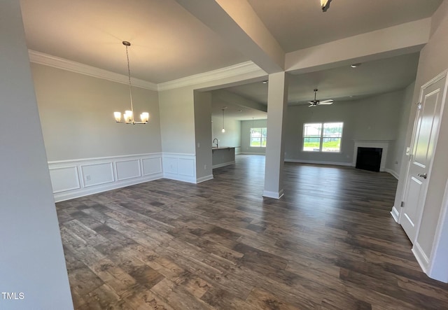 interior space with dark wood-style floors, a wainscoted wall, crown molding, a fireplace, and ceiling fan with notable chandelier