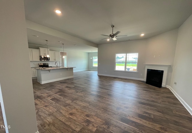 unfurnished living room featuring dark wood-style floors, baseboards, a fireplace, and a sink