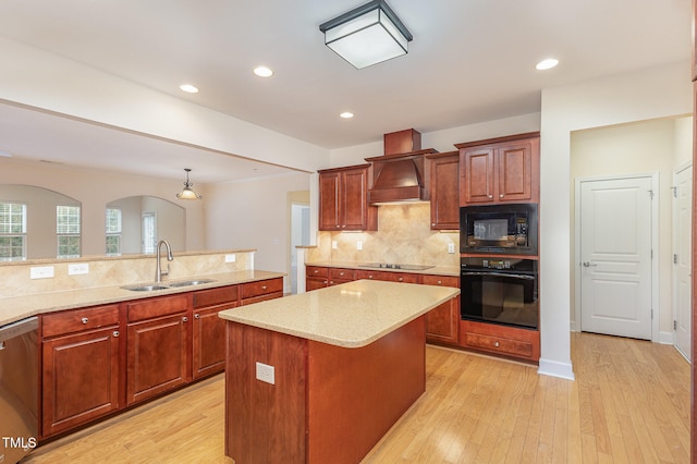 kitchen featuring custom exhaust hood, black appliances, sink, light wood-type flooring, and a kitchen island