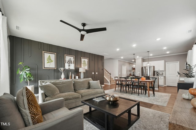 living room with ceiling fan, ornamental molding, and light wood-type flooring