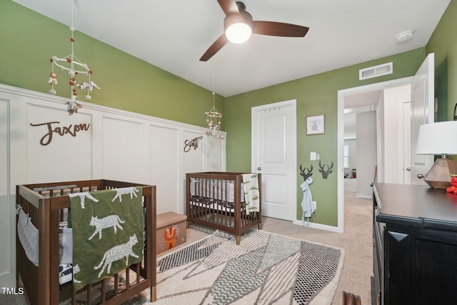 bedroom featuring a crib, ceiling fan, and light colored carpet