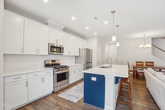 kitchen with stainless steel appliances, sink, a center island with sink, white cabinetry, and hanging light fixtures