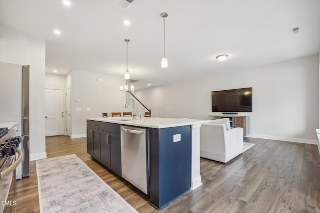 kitchen with sink, dark wood-type flooring, hanging light fixtures, a center island with sink, and appliances with stainless steel finishes