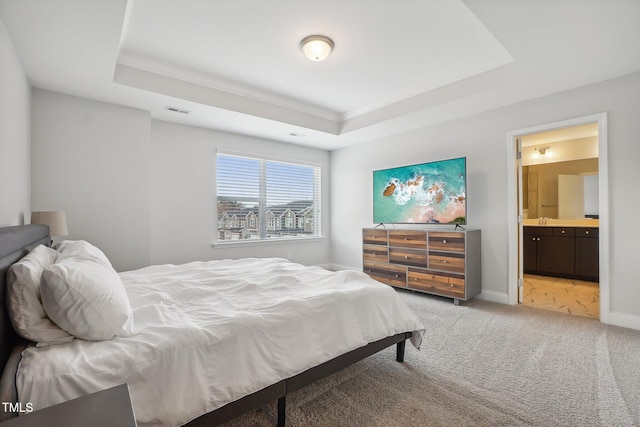 carpeted bedroom with connected bathroom and a tray ceiling