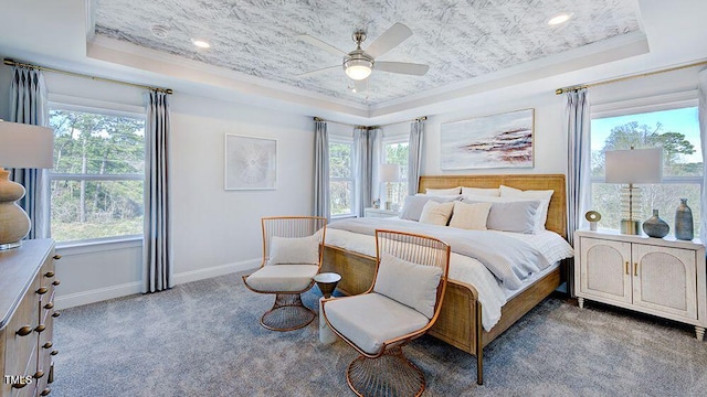 carpeted bedroom featuring a tray ceiling, multiple windows, and ceiling fan