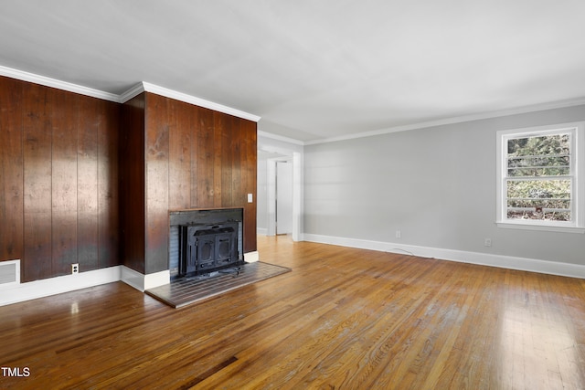 unfurnished living room with light wood-type flooring, wooden walls, a wood stove, and crown molding