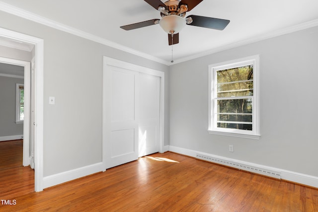 unfurnished bedroom with a baseboard radiator, wood-type flooring, multiple windows, and ceiling fan