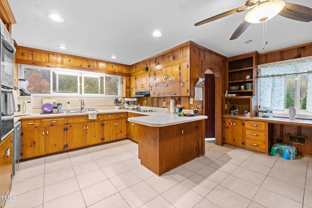 kitchen featuring kitchen peninsula, ceiling fan, sink, light tile patterned floors, and wood walls