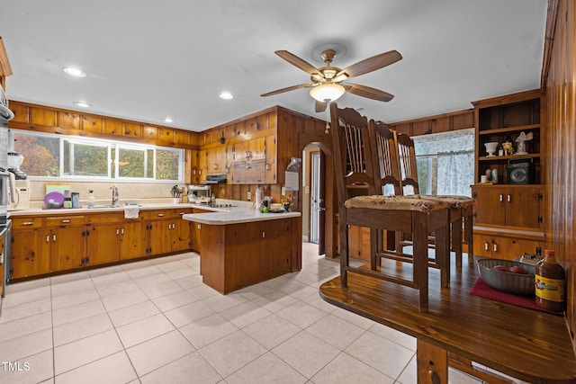 kitchen with wood walls, sink, ceiling fan, light tile patterned floors, and kitchen peninsula