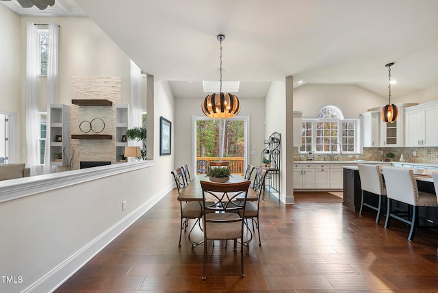 dining space featuring lofted ceiling, an inviting chandelier, a stone fireplace, sink, and dark hardwood / wood-style floors