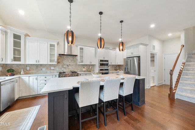 kitchen with pendant lighting, an island with sink, appliances with stainless steel finishes, dark hardwood / wood-style flooring, and white cabinetry