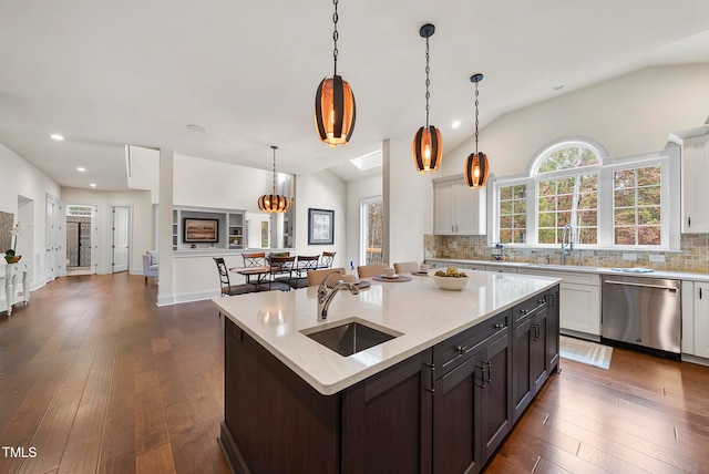 kitchen featuring dark wood-type flooring, stainless steel dishwasher, pendant lighting, vaulted ceiling with skylight, and a center island with sink