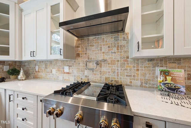 kitchen featuring white cabinets, backsplash, light stone countertops, and range hood