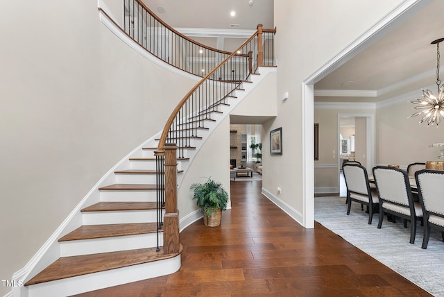 stairs with a chandelier, wood-type flooring, a towering ceiling, and ornamental molding