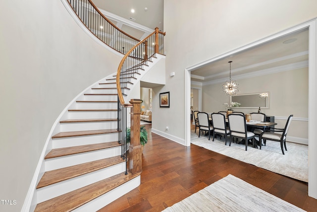 stairway with wood-type flooring, a towering ceiling, an inviting chandelier, and crown molding