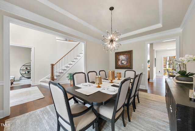 dining space featuring a chandelier, wood-type flooring, a raised ceiling, and ornamental molding